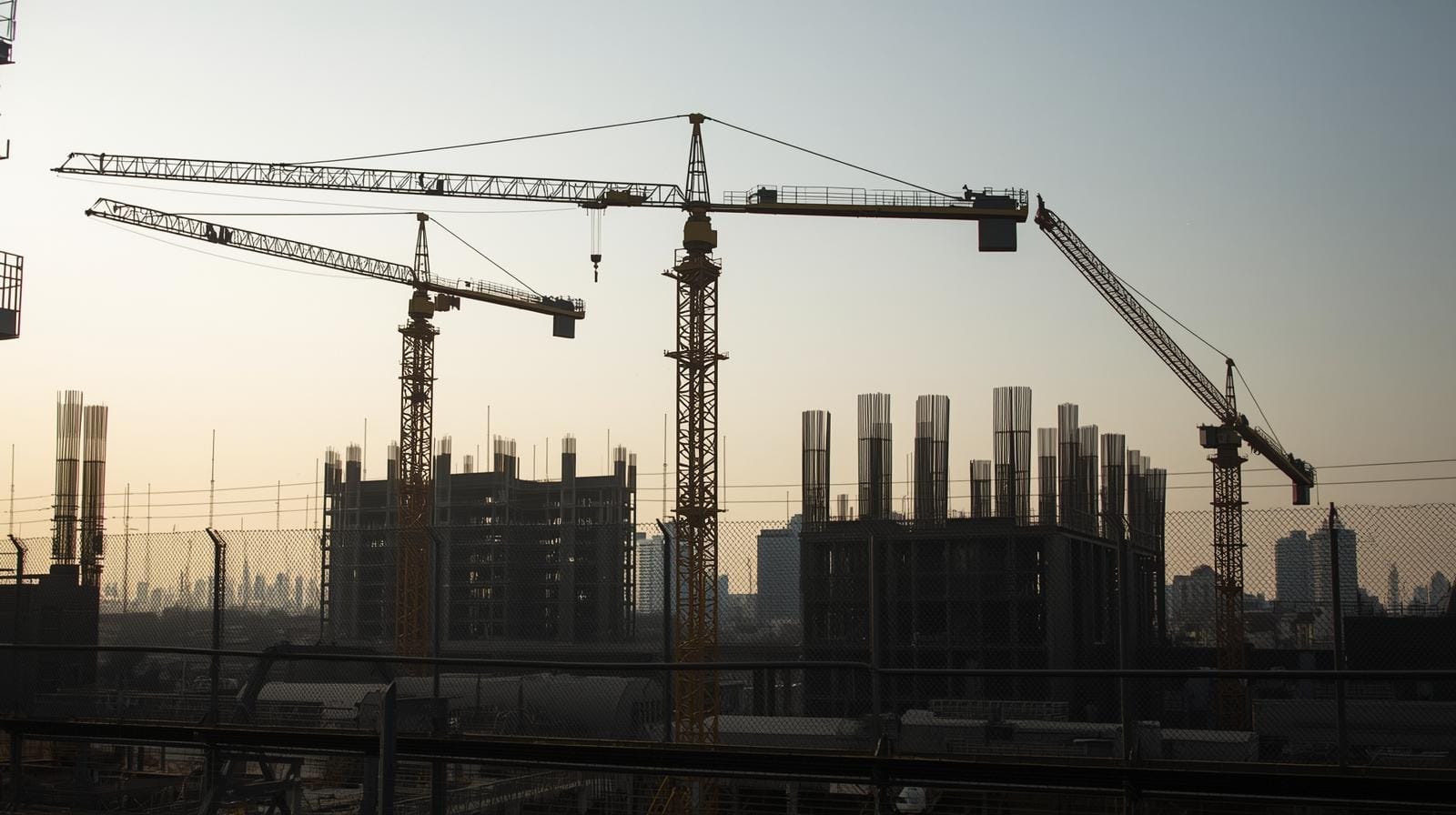 A halted condo construction site in Bangkok with inactive cranes and unfinished structures, showing how developers are freezing new projects amid financial pressures.
