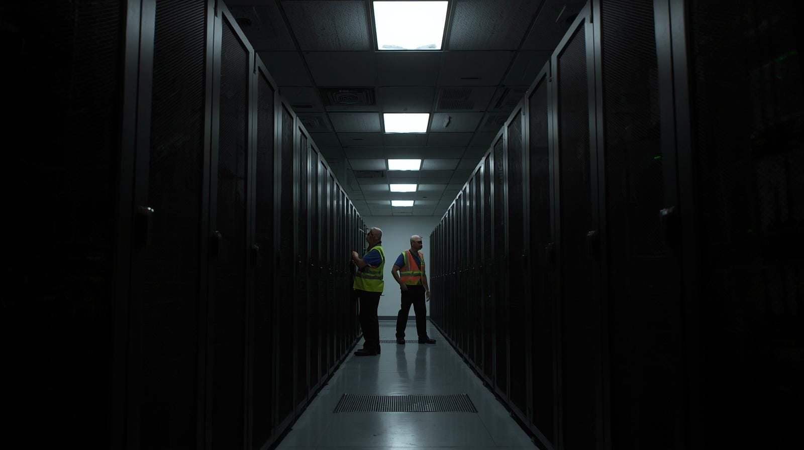 Interior of a dimly lit data hall with server racks and staff inspecting equipment during a simulated power issue.